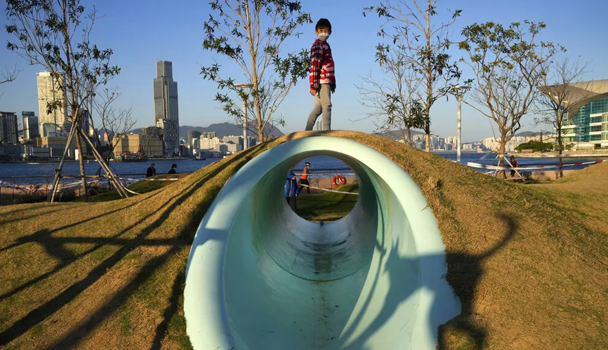 Seorang anak laki-laki yang mengenakan masker bermain di sebuah taman di Hong Kong, 8 Maret 2022. Pemerintah Hong Kong memperluas langkah-langkah jarak sosial, memaksa banyak fasilitas bisnis dalam ruangan seperti pusat kebugaran, salon, bar, dan spa tutup. (AP Photo/Kin Cheung)