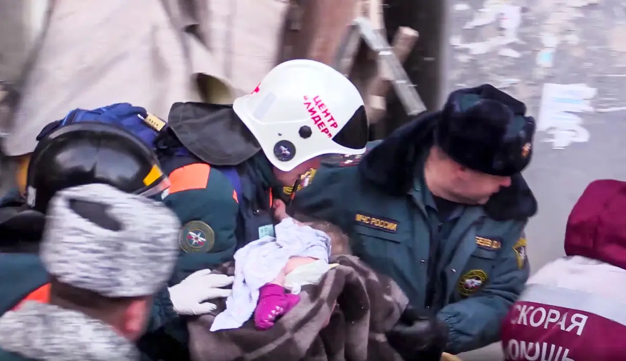 Tim penyelamat menggendong bayi yang ditemukan tertimbun reruntuhan gedung apartemen yang ambruk di Magnitogorsk, Rusia, Selasa (1/1). Bayi itu segera dibungkus selimut dan dievakuasi ke rumah sakit. (Russian Ministry for Emergency Situations via AP)