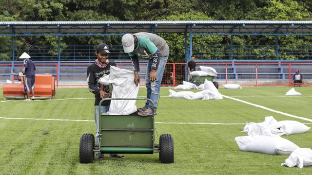 Para pekerja merapihkan rumput sintetis di Lapangan Aldiron. (Bola.com/M. Iqbal Ichsan)