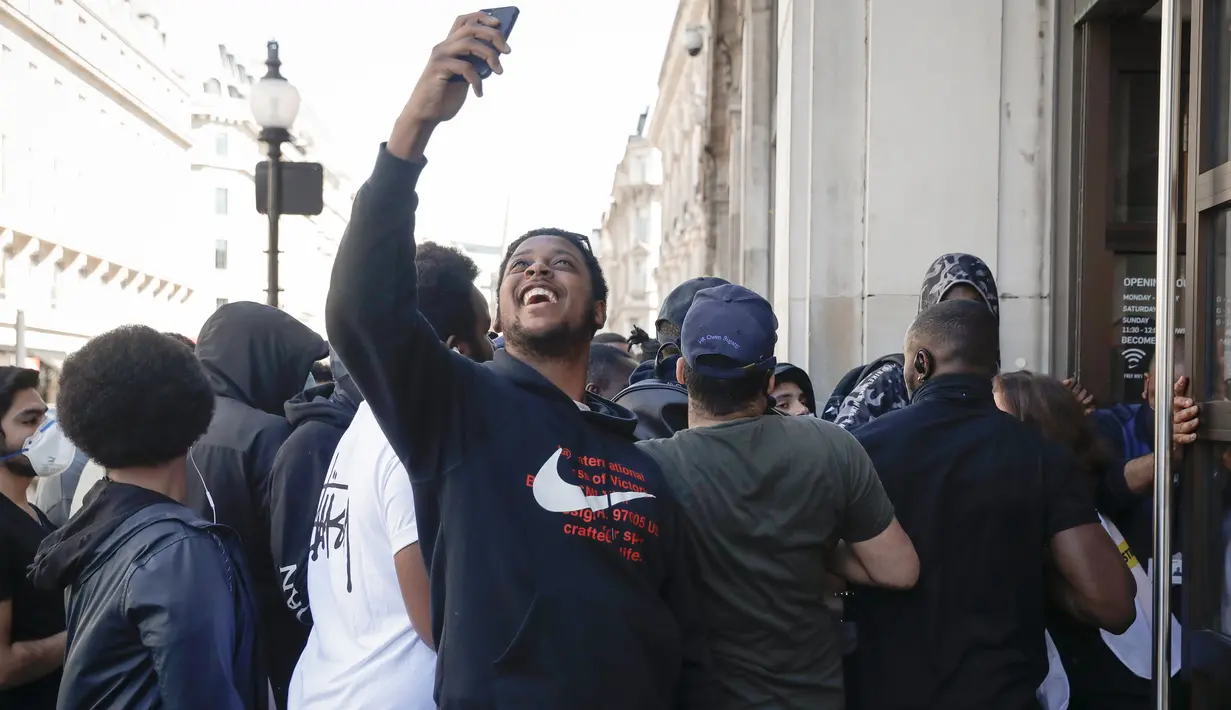 Seorang pemuda mengambil foto ketika orang-orang antre untuk memasuki toko Niketown di London, Senin (15/6/2020). Antrean panjang terjadi di luar toko-toko yang berada di sejumlah kota di Inggris saat negara itu melakukan pelonggaran lockdown dan mulai membuka pusat perbelanjaan. (AP/Matt Dunham)