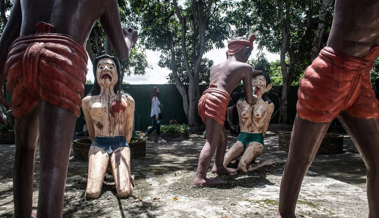 Seorang wanita berjalan di dekat patung-patung yang menggambarkan nasib orang-orang yang melakukan perbuatan buruk di taman yang menggambarkan neraka versi Buddha di kuil Wat Saeng Suk di provinsi pantai Thailand Chonburi (9/7/2020). (AFP/Lillian Suwanrumpha)