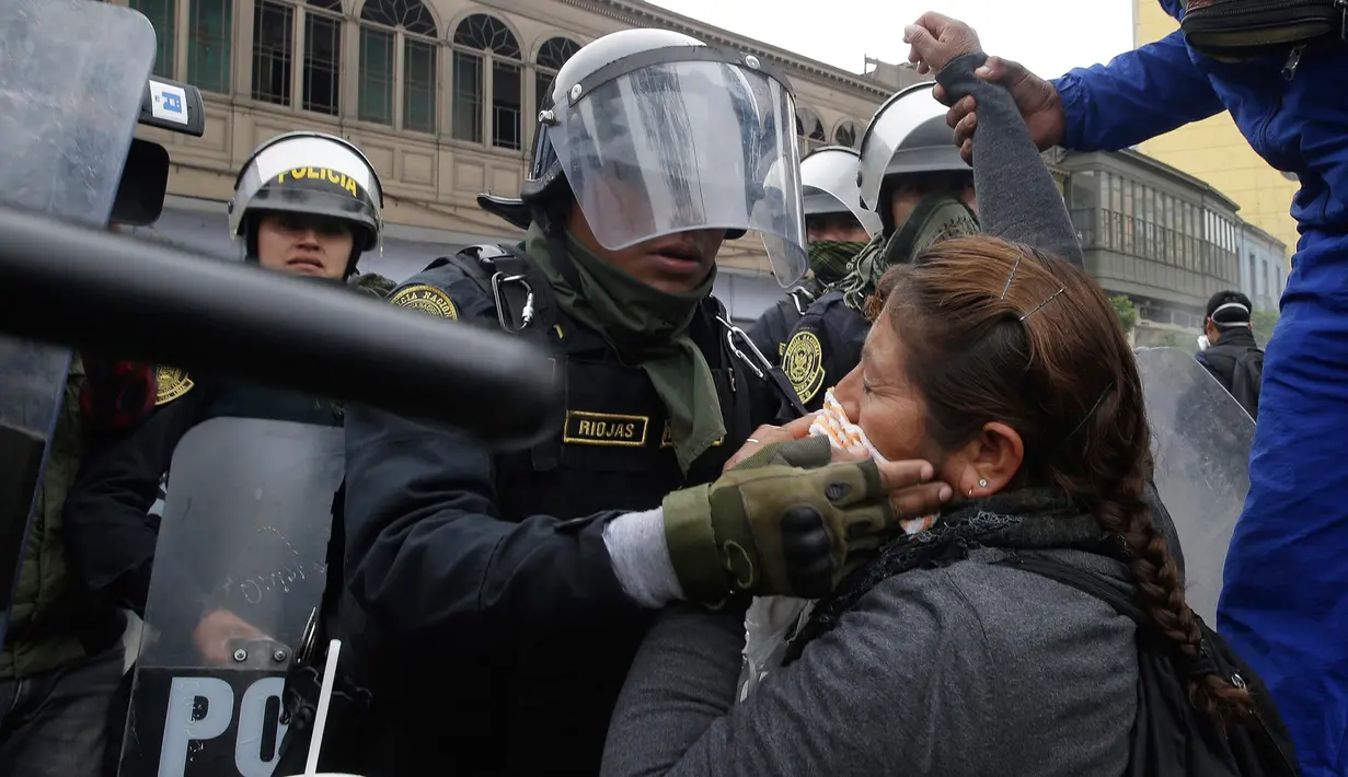 Petugas polisi membantu seorang guru yang terkena gas air mata saat unjuk rasa di Lima, Peru,  (24/8). Sejumlah  Guru sekolah umum menuntut kenaikan gaji. (AP Photo / Martin Mejia)