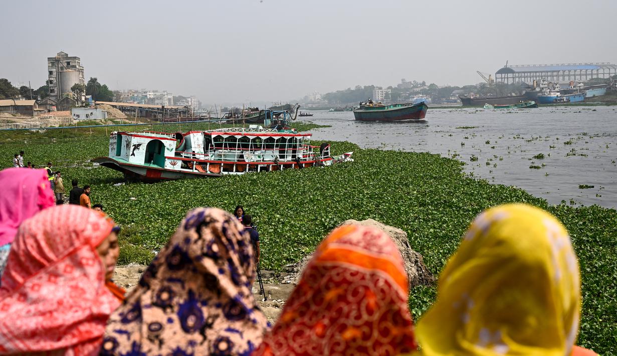 Orang-orang menonton feri yang diselamatkan setelah kecelakaan di Sungai Shitalakshya di Narayanganj, Bangladesh (21/3/2022). Setidaknya enam mayat ditemukan dan 20 orang masih hilang setelah sebuah feri terbalik di sungai Shitalakkhya. (AFP/Munir uz Zaman)