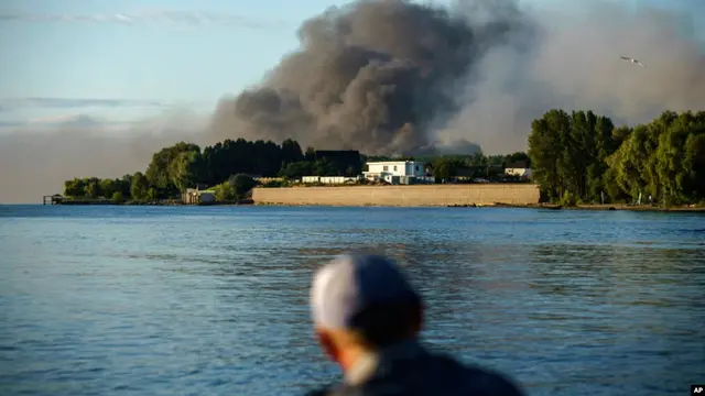 Seorang nelayan mengamati asap yang mengepul di seberangnya setelah pasukan Rusia melancarkan serangan misil ke Distrik Vyshhorod, di pinggiran Kota Kiev, Ukraina, pada 28 Juli 2022. (Foto: AP/David Goldman)