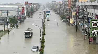 Orang-orang dan kendaraan menyeberangi air di sepanjang jalan yang tergenang banjir akibat Topan Gaemi di Kaohsiung, Taiwan pada tanggal 25 Juli 2024. ((Johnson LIU/AFP)