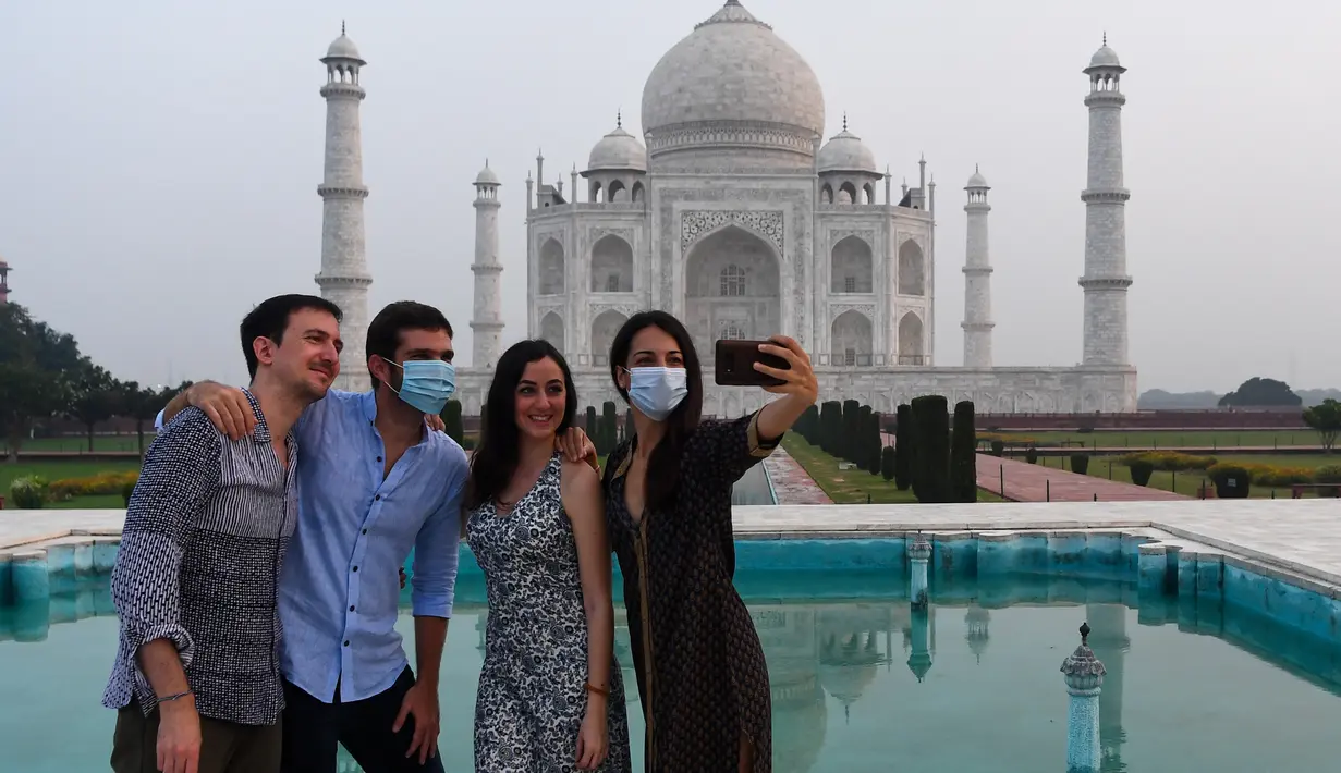Turis berfoto dengan latar belakang Taj Mahal di Agra, India pada Senin (21/9/2020). Taj Mahal kembali dibuka untuk umum hari ini, Senin (21/9), saat negara dengan 1,3 miliar orang itu telah mencatat lebih dari 5,4 juta kasus Covid-19. (Sajjad HUSSAIN/AFP)