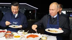 Presiden Rusia Vladimir Putin (kanan) dan Presiden China Xi Jinping (kiri) menyantap pancake buatan bersama di sela acara Eastern Economic Forum di Vladivostok, Rusia, Selasa (11/9). (Sergei Bobylev/TASS News Agency Pool Photo via AP)