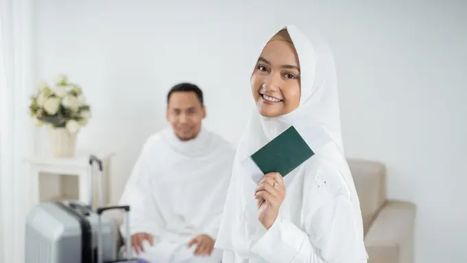 suami istri memakai baju muslim putih membawa paspor
