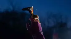 Seorang wanita membantu kelelawar yang diselamatkan untuk kembali terbang saat upacara pengembalian kelelawar ke alam liar di Kyiv, Ukraina, Sabtu 4 April 2026. Ukrainian Bat Rehabilitation Center menggelar upacara pengembalian kelelawar ke alam liar. (AP Photo/Dan Bashakov)