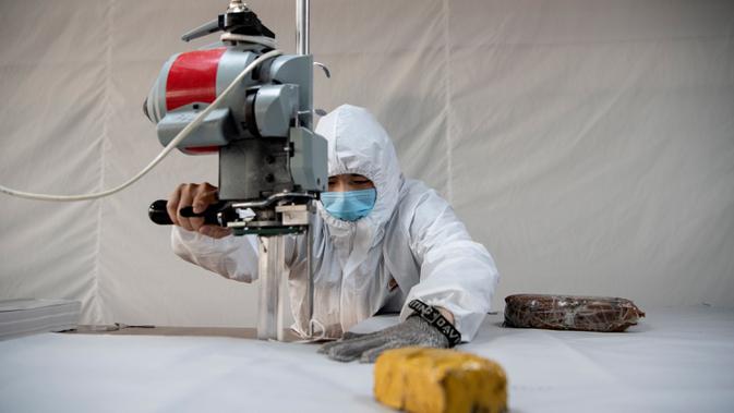 Pekerja memotong bahan untuk digunakan membuat pakaian antivirus di pabrik garmen Zhejiang Ugly Duck Industry, di Wenzhou, 28 Februari 2020. Wabah virus corona di China membuat produsen pakaian itu mulai memproduksi baju hazmat yang banyak diburu orang untuk melindungi dirinya. (NOEL CELIS/AFP)