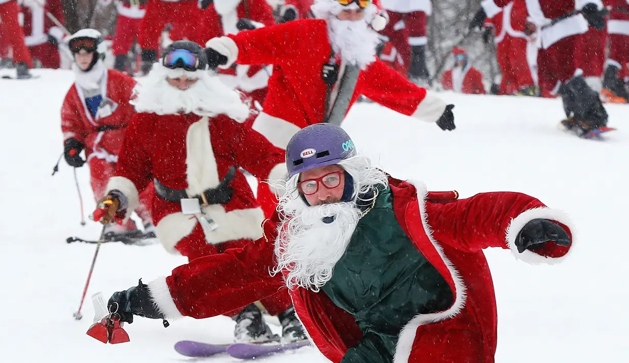 Pemain ski dan snowboarder berpakaian Santa Claus menuruni lereng gunung saat Santa Sunday ke-19 di Newry, Maine, AS, Minggu (2/12). Santa Sunday merupakan acara amal tahunan. (AP Photo/Robert F. Bukaty)