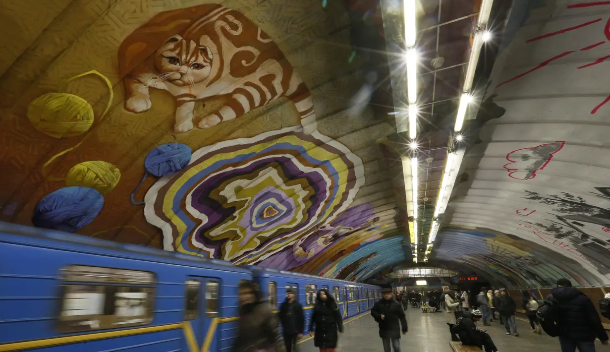 Penumpang melewati kereta di bawah mural yang menghiasi dinding stasiun metro bawah tanah kota di Kyiv, Ukraina, Rabu, (29/1/2020). (AP Photo / Efrem Lukatsky)