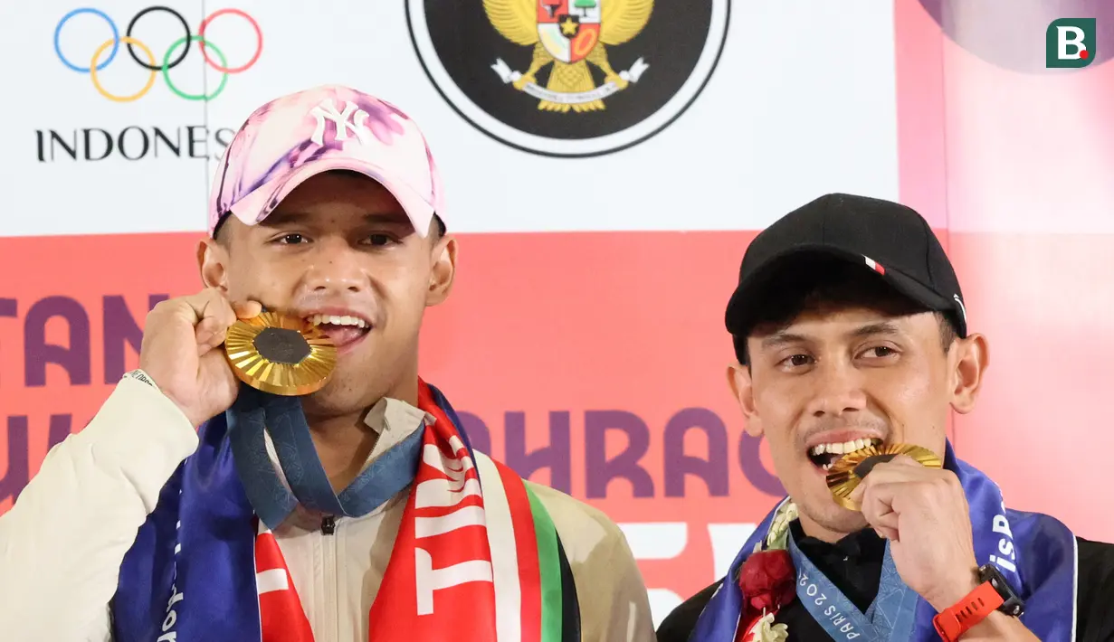 <p>Dua atlet Indonesia peraih medali emas di Olimpiade 2024 Paris Rizki Juniansyah (kiri) dan Veddriq Leonardo (kanan) berpose menggigit medali emasi usai tiba di Bandara Internasional Soekarno-Hatta, Tangerang, Selasa (13/8/2024) (Abdul Aziz/Bola.com).&nbsp;</p>