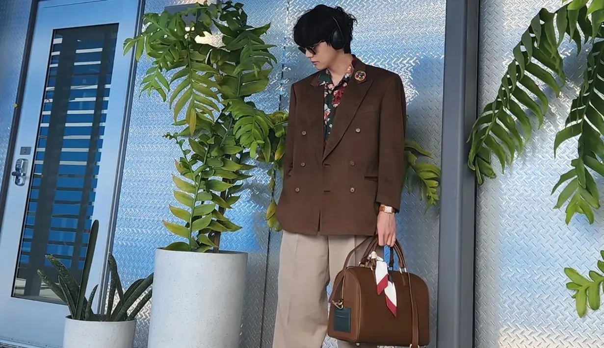 Taehyung dengan outfit berwarna cokelat yang serba serasi. Kemeja bermotif ditumpuknya dengan blazer cokelat, dipadu dengan celana panjang yang senada, sneakers putih, dan ia menenteng tas kulit yang juga berwarna cokelat. Foto: Instagram.