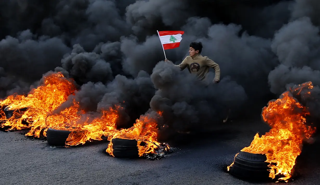 Demonstran antipemerintah melompati ban yang terbakar saat protes menentang elite penguasa di Kota Jal el-Dib, Lebanon, Selasa (14/1/2020). Demonstran menganggap elite penguasa gagal mengatasi ekonomi yang menurun tajam. (AP Photo/Bilal Hussein)