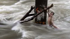 Seorang bocah laki-laki memegang batang pohon saat ia bermain di sungai dengan arus yang sangat deras akibat hujan lebat di bawah jembatan di Manila, Filipina (11/6). (AFP Photo/Noel Celis)