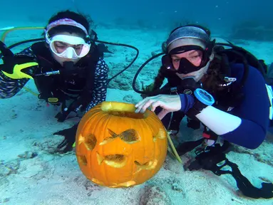 Dua penyelam, Sophie Costa dan Allison Candelmo menunjukkan buah labu dalam Kontes Mengukir Labu Bawah Air, di Cagar Alam Laut Nasional Florida Keys, Florida, Minggu (14/10). Kompetisi diadakan di laut sedalam 9 meter. (Frazier Nivens/various sources/AFP)