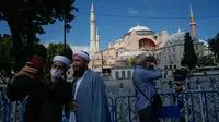 Orang-orang berswafoto dengan latar belakang Hagia Sophia di distrik bersejarah Sultanahmet di Istanbul, 11 Juli 2020. Berubahnya status bangunan yang memiliki kubah ikonik ini menjadi masjid tentu membuat publik heboh. (AP Photo/Emrah Gurel)