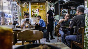 Pelanggan bersantap di sebuah restoran saat pemerintah mengumumkan pelonggaran pembatasan Covid-19 paling ketat, di Hong Kong, Kamis (14/4/2022). Pelonggaran tersebut akan memungkinkan salon kecantikan, bioskop, dan pusat kebugaran dibuka kembali mulai 21 April 2022 mendatang. (ISAAC LAWRENCE/AFP)