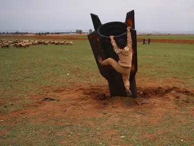 Seorang anak laki-laki mempertaruhkan nyawanya, di tengah bahaya amunisi, dengan mencoba memanjat proyektil Iran yang belum meledak di lapangan terbuka di pinggiran Qamishli, Suriah timur, Rabu 4 Maret 2026. Sebuah proyektil rudal Iran yang belum meledak (unexploded ordnance) mendarat di lapangan terbuka di pinggiran Qamishli, timur laut Suriah. (AP Photo/Baderkhan Ahmad)