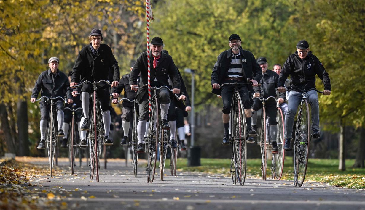 Para penggemar mengenakan pakaian bersejarah mengendarai sepeda yang mereka sebut penny-farthing, atau yang juga dikenal sebagai high wheel, dalam kompetisi tradisional 'One Mile Race' di Taman Letna, Praha, Republik Ceko, pada 1 November 2025. Mereka ikut serta dalam kompetisi tradisional 'One Mile Race'. (Michal Cizek/AFP)