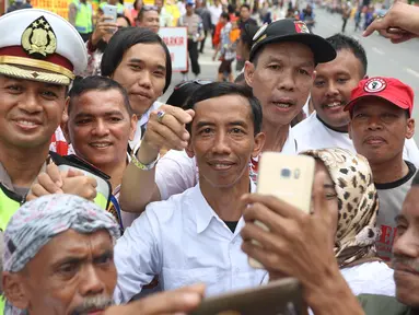 Seorang pria berwajah mirip Presiden Joko Widodo (Jokowi) berswafoto bersama warga yang memadati sekitar Gedung Graha Saba Buana, Solo, Rabu (8/11). Pria bernama David itu beberapa saat berhasil mengecoh warga. (Liputan6.com/Angga Yuniar)