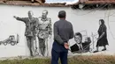 Ivan mengamati mural yang menggambarkan penduduk setempat bersama Pemimpin revolusi Kuba Fidel Castro dan Presiden Amerika Serikat John F. Kennedy di dinding rumah warga di desa Staro Zhelezare, Bulgaria, Kamis (27/7). (AP Photo/Valentina Petrova)