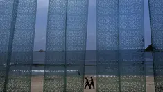 Dua pria terlihat dari tirai plastik sebuah restoran berjalan di pantai Sijung Ho di Korea Utara (14/7/2019). Pantai Sijung Ho merupakan tujuan wisata populer bagi penduduk lokal dan asing. (AP Photo/Vincent Yu)