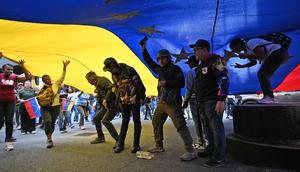 Operasi militer AS berskala besar ini diperintahkan oleh Presiden Donald Trump. Tampak dalam foto, pendukung mantan Presiden Venezuela, Nicolas Maduro, berdemonstrasi dengan bendera nasional raksasa di Caracas pada Minggu 4 Januari 2026. (Juan BARRETO/AFP)