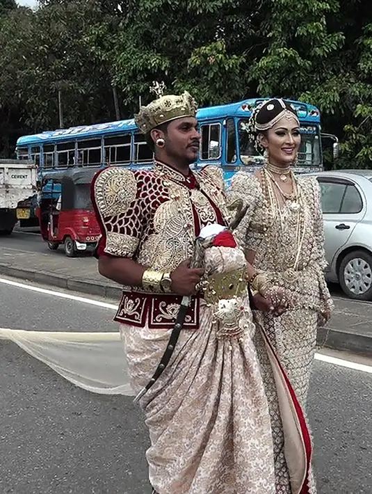 Sepasang pengantin Sri Lanka berjalan menyusuri jalan utama di pusat kota Kandy, 22 September 2017. Pasangan pengantin tersebut diperiksa oleh polisi karena melibatkan sekitar 250 siswa untuk memegang saree atau gaun pengantin pada jam sekolah. (STR/AFP)