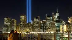 Sepasang kekasih menikmati ‘Tribute in Light’ dari sisi Brooklyn Promenade untuk mengenang tragedi serangan WTC di New York, Minggu (10/9). Kota New York memperingati 16 tahun tragedi serangan bom pada 11 September 2001 silam. (AP Photo/Mark Lennihan)