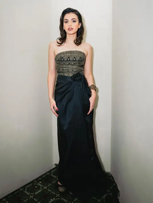 Carmela van der Kruk tampil tak kalah menawan. Di Gala Premiere Catatan Si Boy, ia memilih mengenakan set cropped top hitam dengan sentuhan motif berwarna emas yang glamor, dipadu kain hitam panjang sebagai rok. [Foto: Instagram/carmelavdkruk]