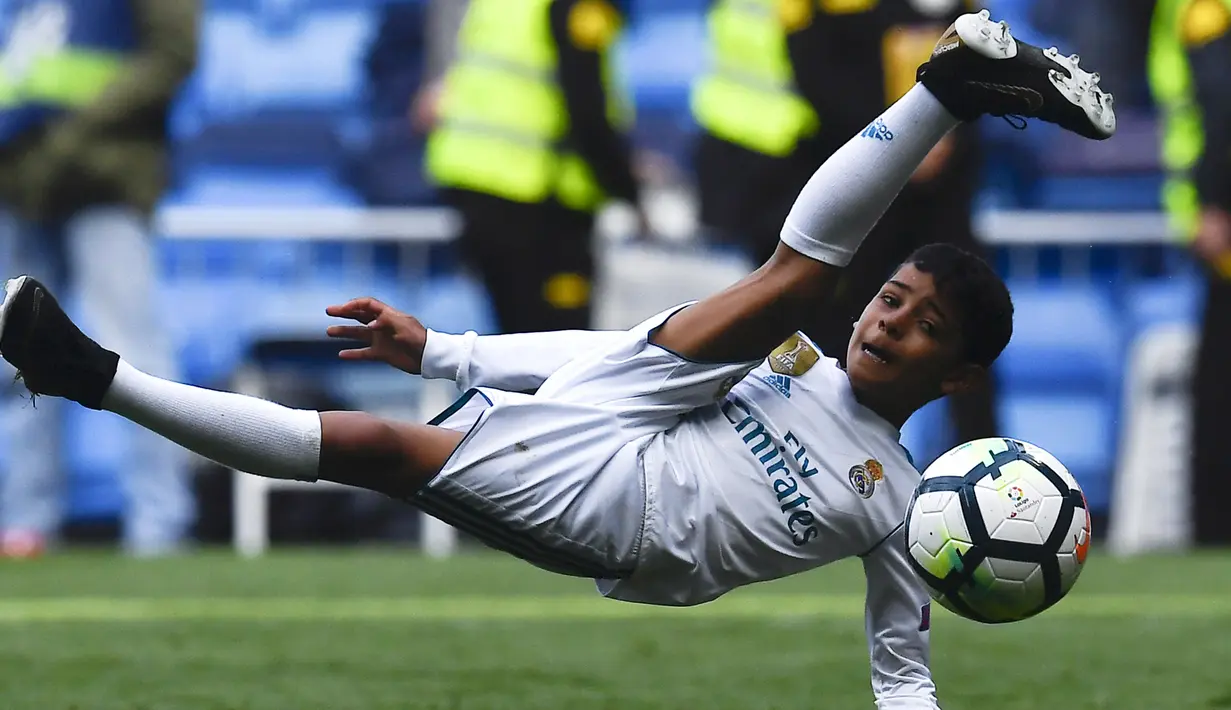 Putra dari Cristiano Ronaldo melakukan tendangan salto saat menemani sang ayah di Stadion Santiago Bernabeu, Madrid, Minggu (8/4/2018). Tendangan ini mirip seperti saat CR 7 membobol gawang Juventus. (AFP/Gabriel Bouys).
