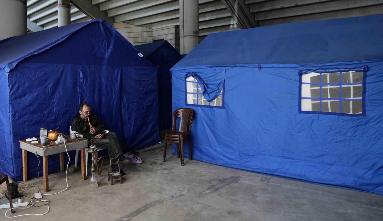 Saat ini, stadion yang sempat terbengkalai akibat kurang perawatan beralih fungsi menjadi tempat penampungan darurat bagi warga untuk menghindari serangan udara Israel. Tampak dalam foto, seorang pengungsi menghisap shisha di samping tenda-tenda yang didirikan di dalam Camille Chamoun Sports City Stadium, yang telah diubah menjadi tempat penampungan bagi orang-orang yang melarikan diri dari serangan udara Israel di Lebanon selatan, Beirut, Lebanon, Rabu 8 April 2026. (AP Photo/Bilal Hussein)