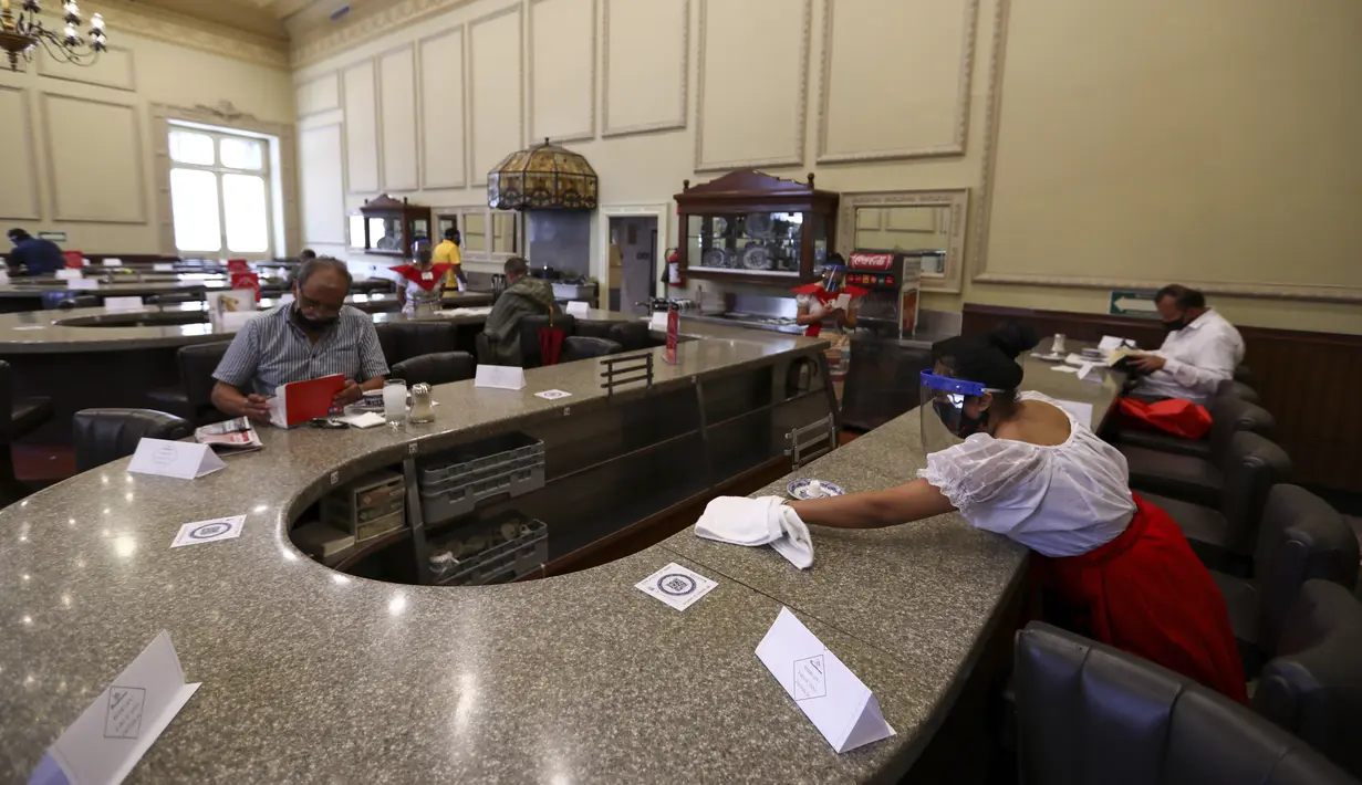 Pelayan mengenakan masker dan pelindung wajah untuk mencegah penyebaran virus corona COVID-19 saat membersihkan meja di Restoran Sanborns of the Azulejos, Mexico City, Meksiko, Rabu (1/7/2020). (AP Photo/Eduardo Verdugo)