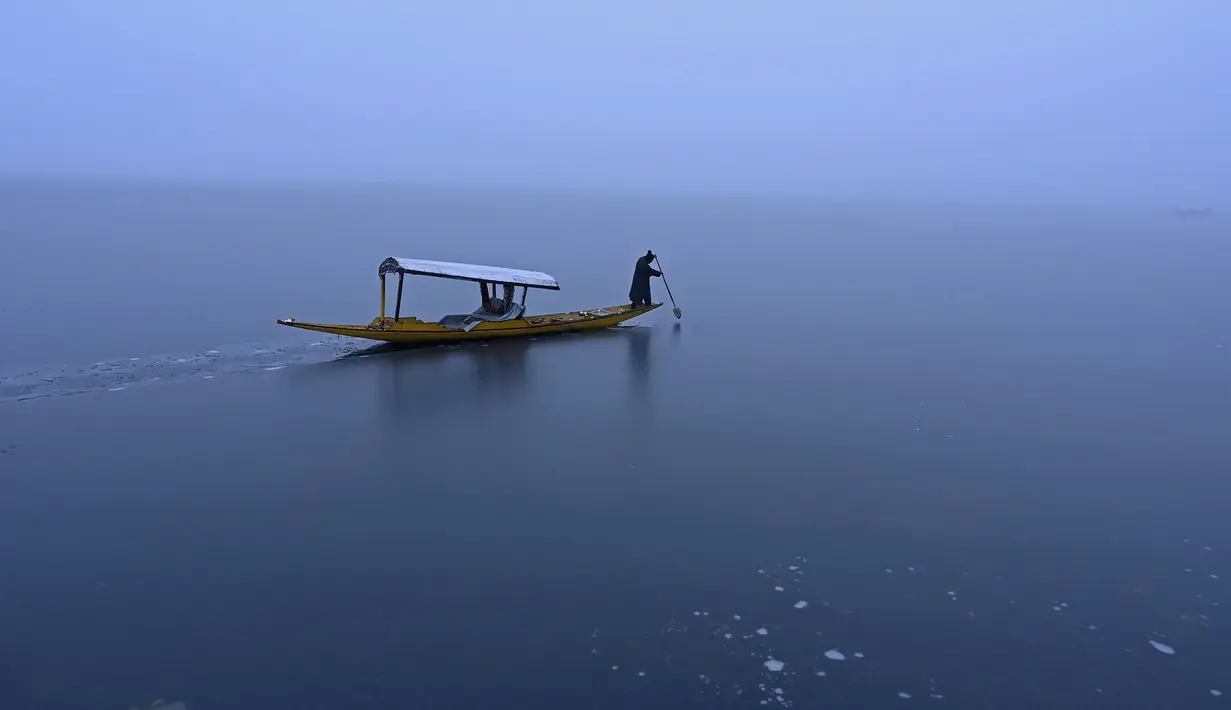 Seorang pria mengendarai perahu di dekat bagian beku danau Dal setelah hujan salju lebat di Srinagar (16/1/2020). Banyak daerah terpencil di lembah telah terputus akibat hujan salju lebat tersebut. (AFP Photo/Tauseef Mustafa)