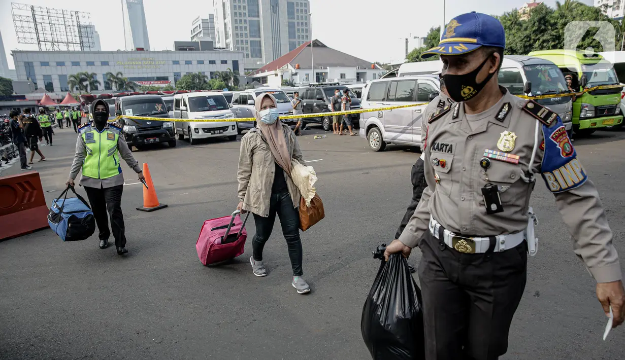 Polisi membantu membawakan barang penumpang yang terjaring razia travel gelap Ditlantas Polda Metro Jaya saat akan dipulangkan ke daerah asalnya, Jakarta, Kamis (29/4/2021). Sebanyak 115 kendaraan travel gelap diamankan. (Liputan6.com/Faizal Fanani)
