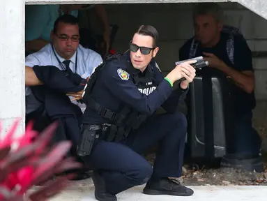 Seorang petugas polisi berlindung di bawah tangga saat memburu pelaku penembakan di Bandara Fort Lauderdale, Florida, AS (6/1). Pelaku penembakan di bandara Florida menewaskan 5 orang. (David Santiago/El Nuevo Herald via AP)