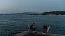 Orang-orang menikmati malam di sebelah pantai Bosphorus ketika jembatan Fatih Sultan Mehmet terlihat di Istanbul (6/7/2020). Jembatan Fatih Sultan Mehmet, yang dikenal dengan sebutan Jembatan Bosporus Kedua, adalah sebuah jembatan di Istanbul, Turki yang melintasi selat Bosporus. (AFP/Ozan Kose)