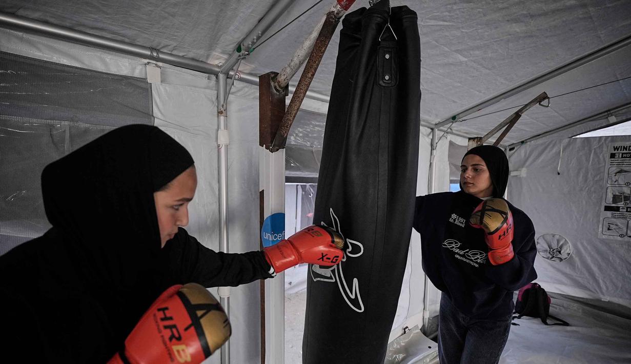 Selanjutnya, mereka memukul samsak seadanya yang digantung pada tiang penyangga tenda, seringkali tanpa sarung tangan tinju. Tampak dalam foto, gadis-gadis Palestina berlatih di klub tinju sementara di dalam tenda di Kota Gaza, Selasa, 5 Mei 2026. (AP Photo/Jehad Alshrafi)