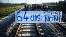 Pengunjuk rasa berdiri di rel kereta api di belakang spanduk bertuliskan "64 tahun, tidak" dalam sebuah aksi yang diserukan oleh serikat pekerja Prancis, Konfederasi Umum Buruh (CGT), untuk memprotes perombakan pensiun di Donges, Prancis Barat, Rabu (8/2/2023). Prancis bersiap menghadapi pemogokan baru dan demonstrasi massal menentang proposal Presiden Prancis untuk mereformasi pensiun Prancis, termasuk menaikkan usia pensiun dari 62 menjadi 64 tahun. (LOIC VENANCE/AFP)