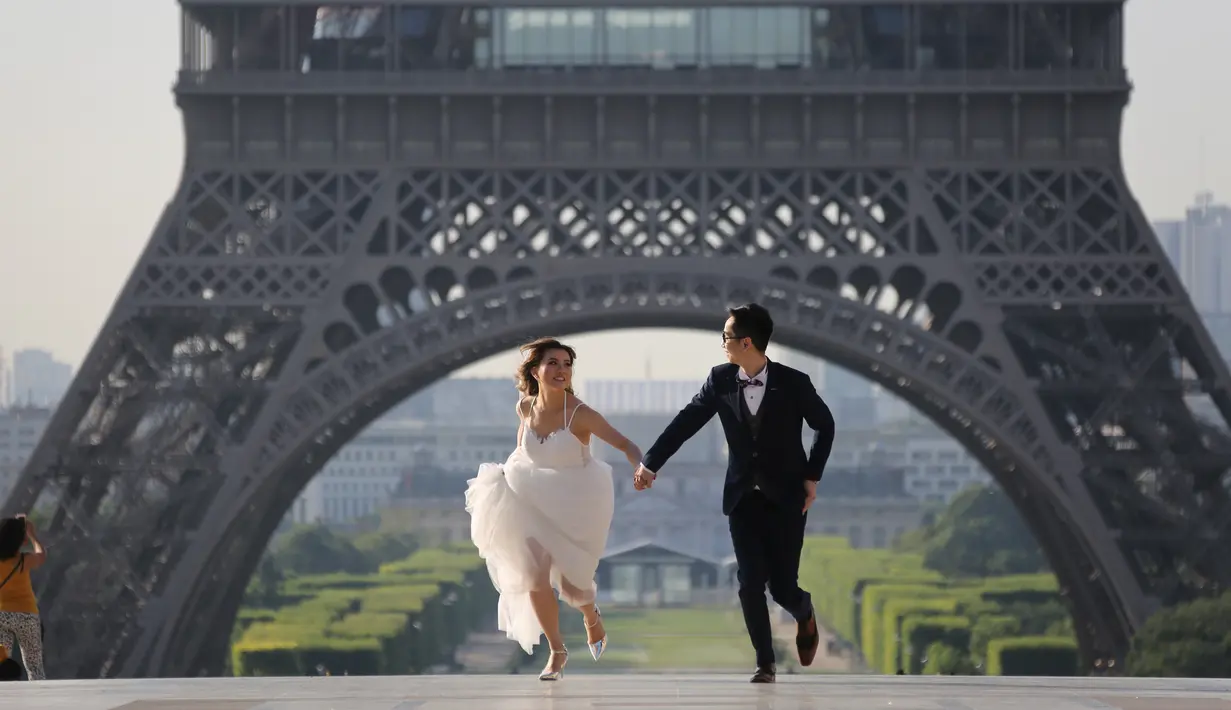 Sepasang calon pengantin berlari ketika melakukan foto prewedding di alun-alun Trocadero di Paris, 4 Juli 2017. Trocadero ini tepat terletak antara Menara Eiffel dan Sungai Seine. (AFP PHOTO / LUDOVIC MARIN)