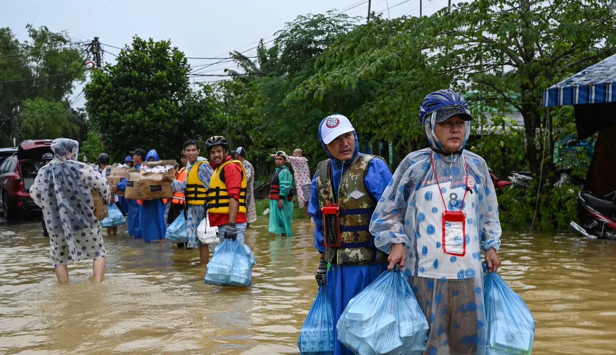 Orang-orang membawa makanan sambil berdiri di jalanan yang terendam banjir setelah hujan deras di Hoi An, Vietnam, Kamis 30 Oktober 2025. Pihak berwenang setempat terus melakukan upaya evakuasi ribuan penduduk dan wisatawan karena meluapnya Sungai Hoai, yang melintasi Hoi An. (NHAC NGUYEN/AFP)