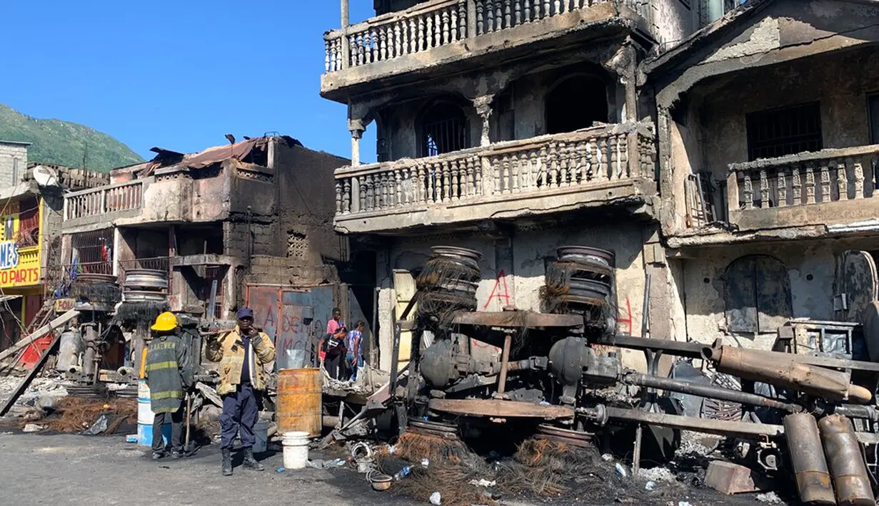 Petugas pemadam kebakaran berdiri dekat bangkai truk pengangkut BBM yang terbalik dan meledak di Cap-Haitien, Haiti, 14 Desember 2021. Menurut Wakil Wali Kota Cap-Hatien Patrick Almonor, ledakan telah menewaskan 62 orang dan melukai puluhan lainnya. (AP Photo/Joseph Odelyn)