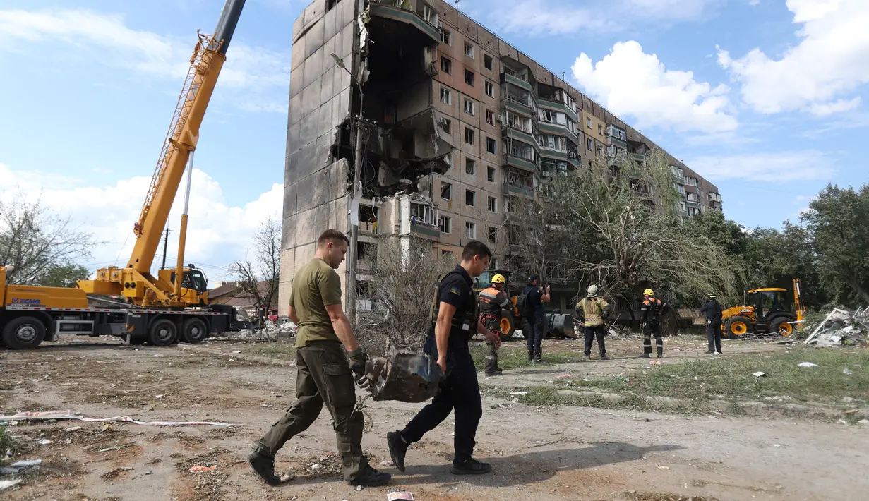 Tim penyelamat membawa pecahan rudal di luar bangunan perumahan sembilan lantai yang sebagian hancur akibat serangan rudal Rusia di Rig Kryvyi pada 31 Juli 2023, di tengah invasi Rusia ke Ukraina. (AFP/Ukrainian Emergency Service)