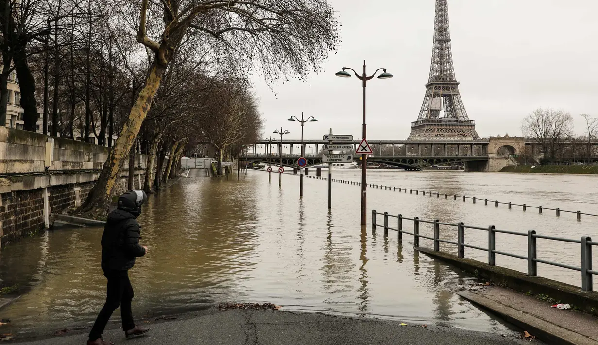Seorang pria berdiri di tepi sungai Seine di dekat menara Eiffel dan distrik Beaugrenelle, Paris (23/1). Sejumlah kapal di sungai tidak dapat berlayar melewati jembatan kota. (AFP Photo/Ludovic Marin)