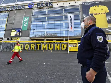 Petugas Keamanan dengan menggunakan masker berjaga di depan Stadion Signal Iduna Park, Jerman, Sabtu (4/4/2020). Stadion Borussia Dortmund ini dialihfungsikan menjadi tempat pusat pengujian COVID-19. (AP/Martin Meissner)