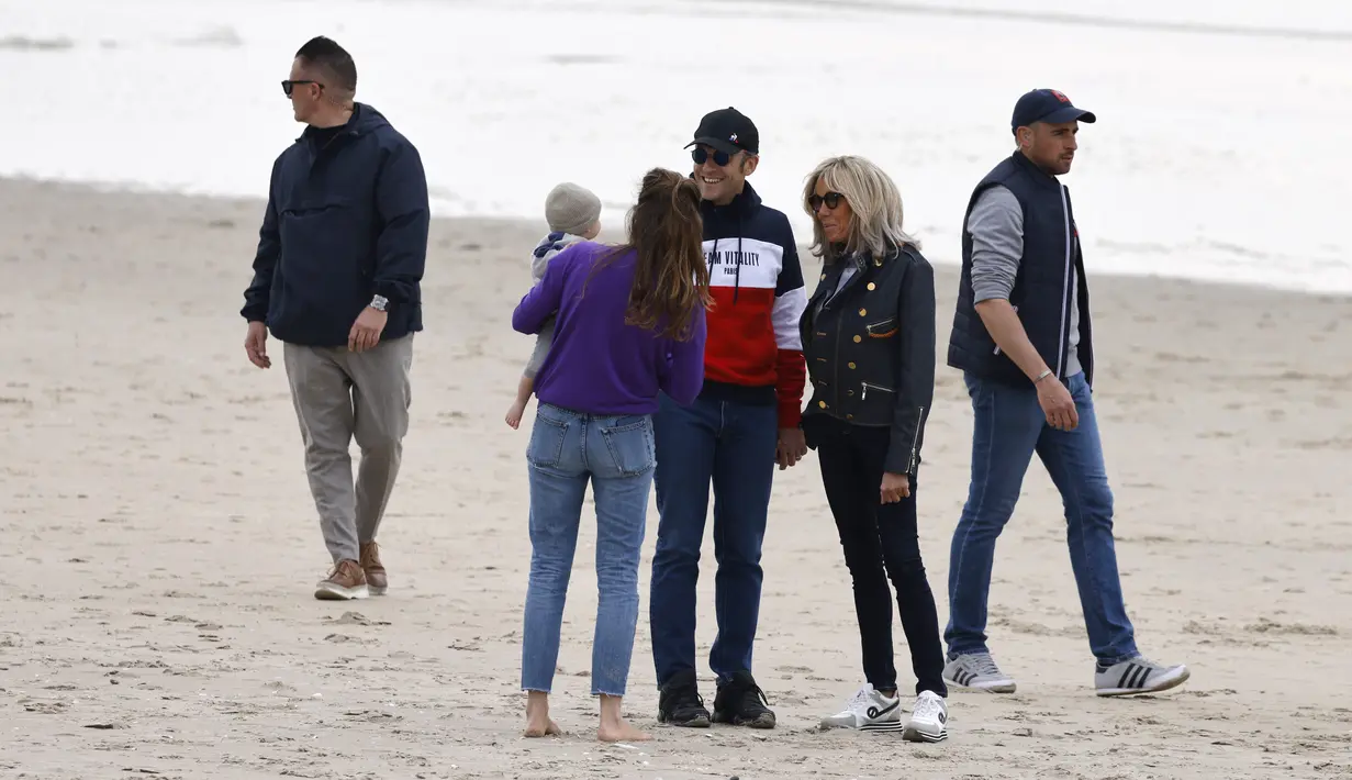 <p>Presiden Prancis Emmanuel Macron dan istrinya Brigitte Macron berbincang dengan seorang wanita yang menggendong anaknya saat mereka berjalan di sepanjang pantai di Le Touquet, Sabtu (23/4/2022). Emmanuel Macron akan menghadapi Marine Le Pen dalam putaran kedua pemilihan presiden (pilpres) pada 24 April 2022. (Ludovic MARIN / AFP)</p>