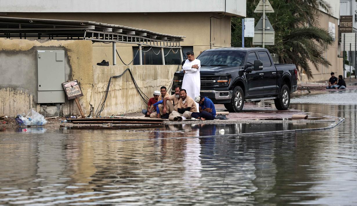Peringatan tersebut datang beberapa jam setelah hujan menyebabkan banjir di jalan-jalan. Tampak dalam foto, para pria duduk menunggu dimulainya salat Jumat siang di tempat yang lebih tinggi sementara air banjir mengalir setelah hujan lebat, di Dubai, Uni Emirat Arab (UEA) pada Jumat 19 Desember 2025. (FADEL SENNA/AFP)