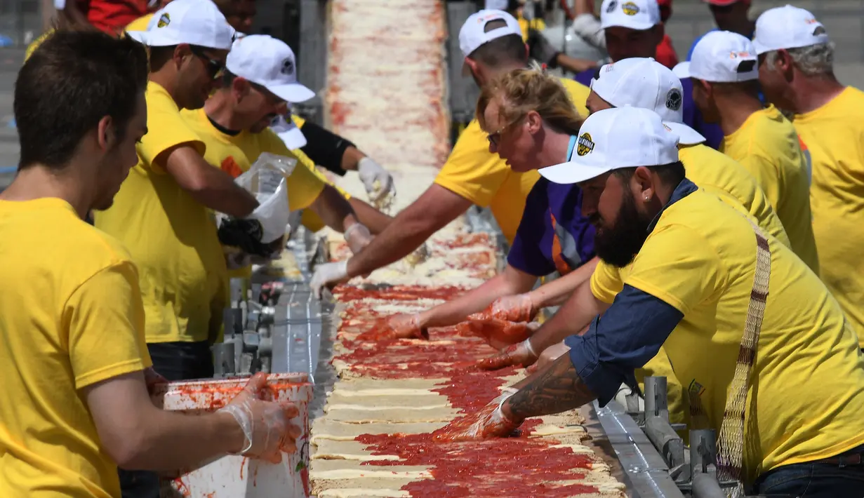Sejumlah peserta mengoleskan saus tomat saat membuat pizza panjang di jalur Auto Club Speedway, di Fontana, California (10/6). (AFP/Mark Ralston)